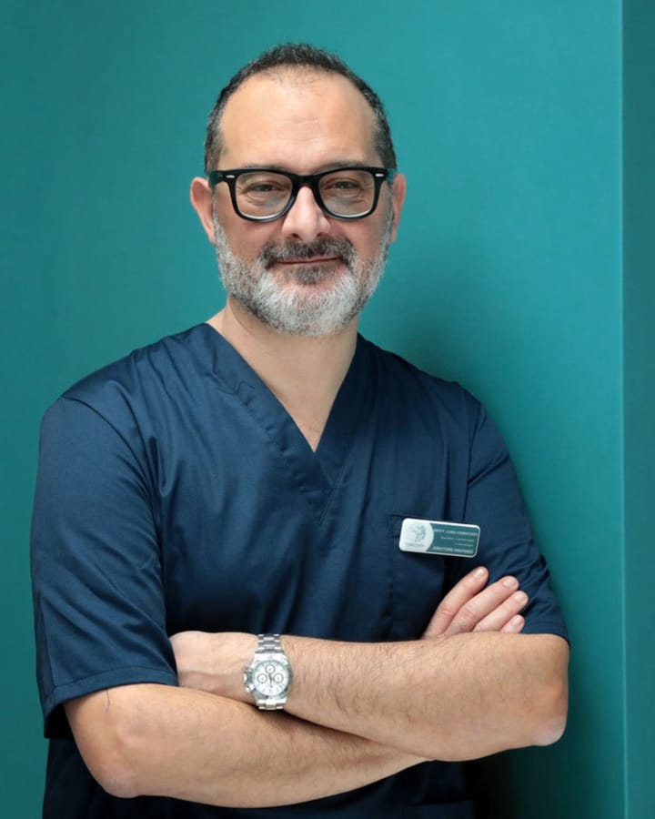 Il Prof. Luigi Coricciati in casacca blu, a braccia conserte, davanti alla parete color petrolio