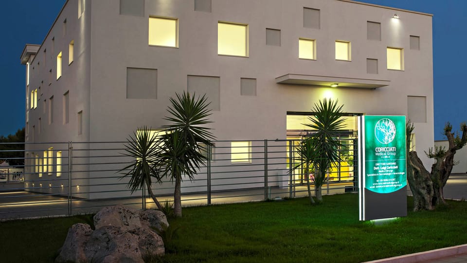 La sede del gruppo a Martano all’ora blu: l’edificio bianco con le finestre accese, le palme, gli ulivi e il totem luminoso